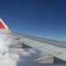 Image contains a photo of the wing of a plane with a blue sky above it and clouds below.