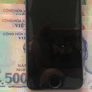 Image contains a photo of an iPhone 5s on top of a number of bills in Vietnamese currency.