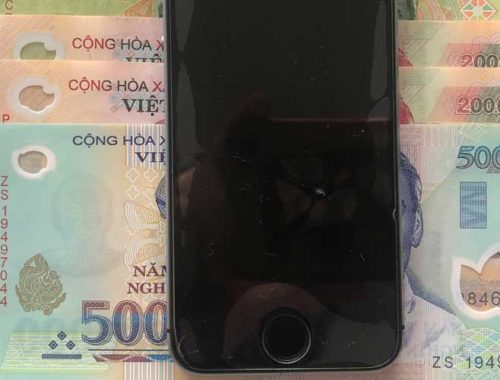 Image contains a photo of an iPhone 5s on top of a number of bills in Vietnamese currency.