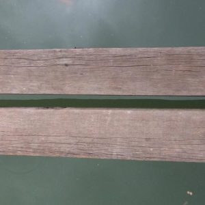 Image contains a photo of two thin wooden boards spanning the length of the image horizontally. Below the boards, there is dark green water. On the right-hand side of the image, two feet can be seen pointing across the boards.