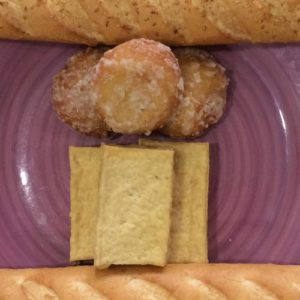 Image contains a photo of a purple plate with blocks of tofu and sugared balls on it. On opposite sides of the plate, there are two baguettes.