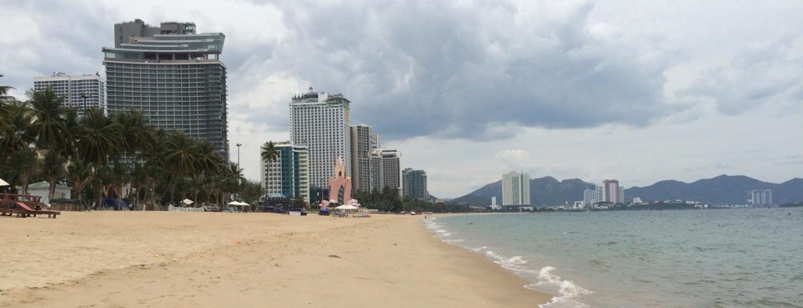 Image contains a photo of a beach with sand on the left and the ocean on the right. In the background, a number of large hotels can be seen.