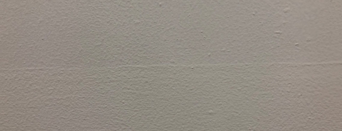 Image contains a photo of a painted white wall with small bumps and a thin line going across the middle.